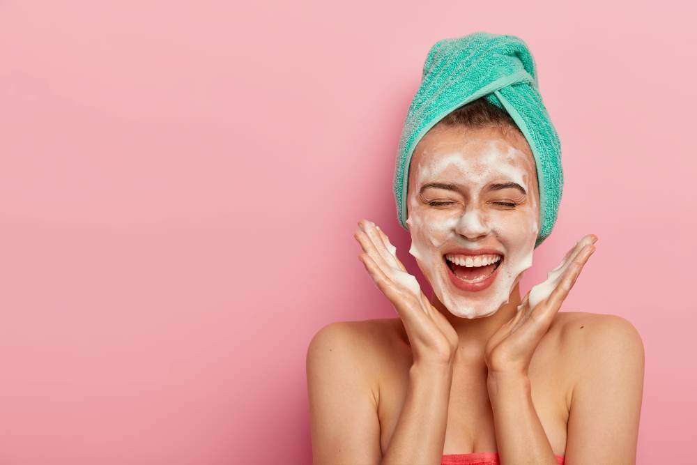 <a href="https://www.freepik.com/free-photo/happy-joyous-young-girl-spreads-palms-face-washes-face-with-soap-has-fun-bathroom-pampers-skin-wears-wrapped-towel-head-expresses-positive-emotions_12838411.htm#query=skincare%20cleansing&position=7&from_view=search&track=ais">Image by wayhomestudio</a> on Freepik